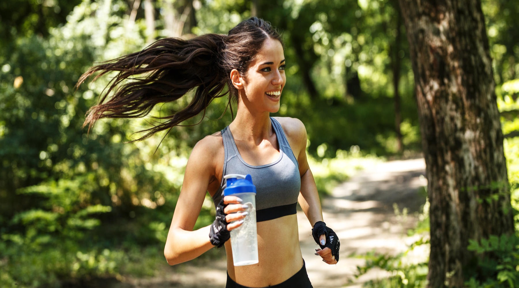 Lady running through woods with water bottle.
